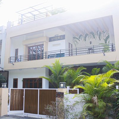Modern two-story residential house with balconies, a wooden gate, and green palm plants.
