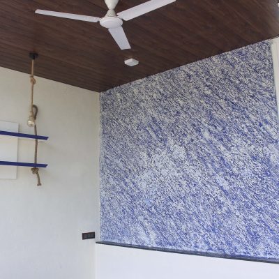 Modern room interior with a blue textured accent wall, wooden ceiling paneling, and a hanging rope shelf.