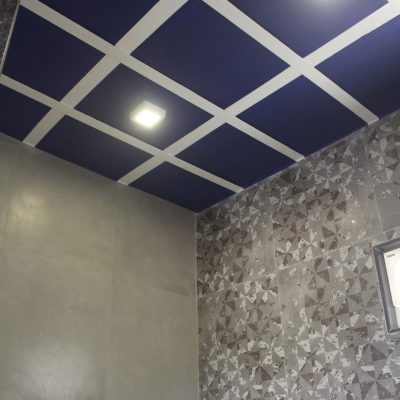Modern false ceiling design with blue and white grid panels, recessed lights, and gray patterned wall tiles.