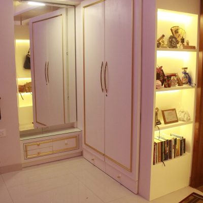 White and gold bedroom wardrobe set next to an illuminated built-in display bookshelf.