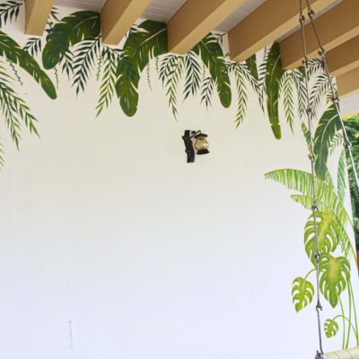 White balcony wall painted with tropical palm leaves and monstera plant mural art.