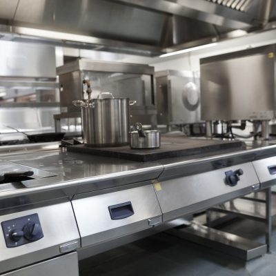 Stainless steel commercial kitchen with industrial cooking equipment, pots, and ovens.