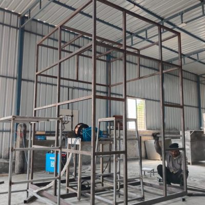 Welded metal structural frame under construction by a worker in a fabrication workshop.