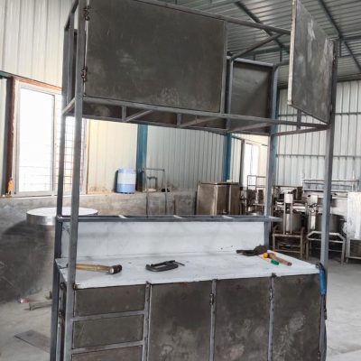 Unfinished metal food cart frame with storage cabinets under construction in a workshop.
